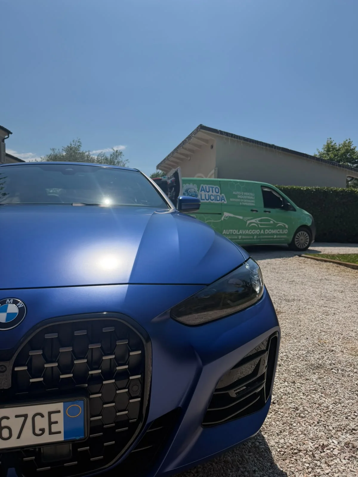 BMW scura in primo piano con furgone verde Auto Lucida sullo sfondo